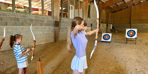 Camper drawing a bow at the archery target in the covered range