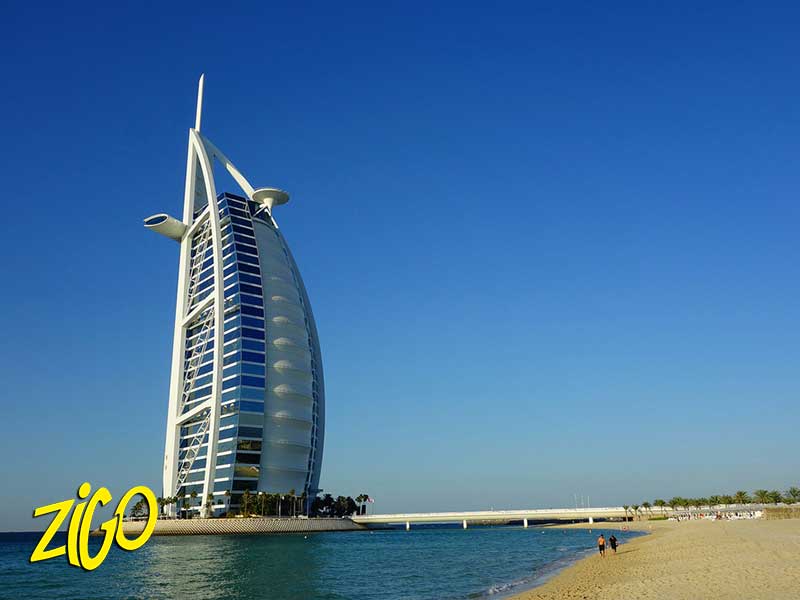 The sail-shaped Burj Al Arab hotel standing on its island across the water under a clear sky