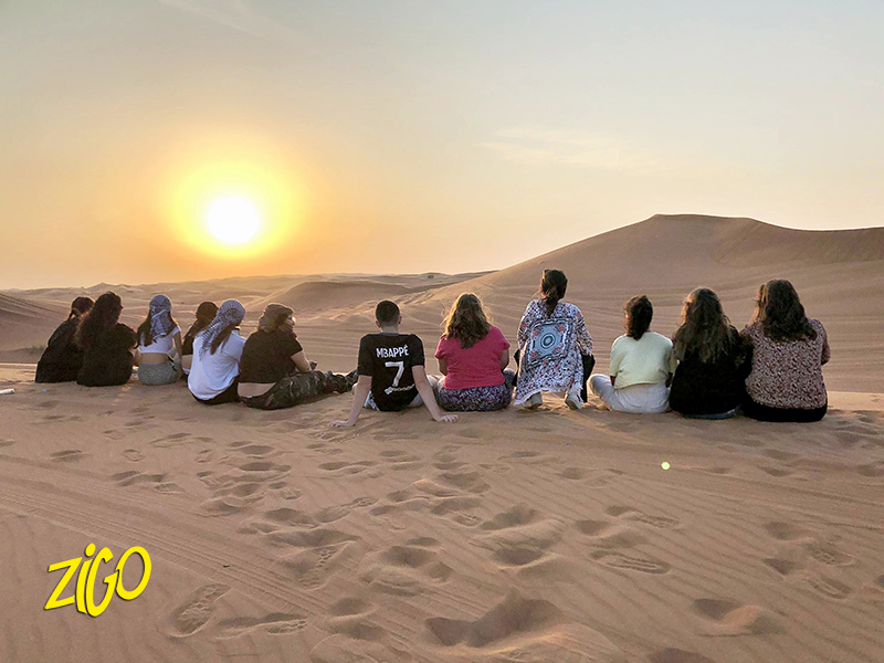 The group sitting together on the crest of a dune watching the sun set over the desert