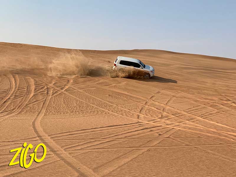 A four-wheel-drive vehicle throwing up a spray of sand as it crosses a dune in the desert