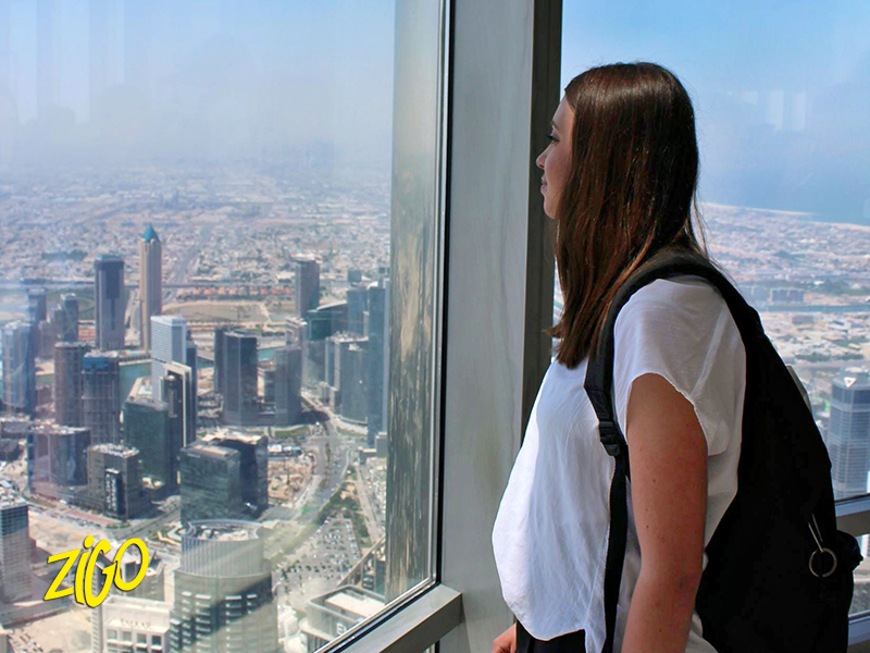 A participant at a floor-to-ceiling window looking out over Dubai's high-rise skyline from high up a tower